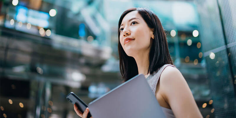 A Women Holding Laptop and Mobile is looking at sky