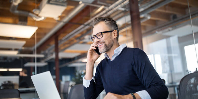 A man is talking in the phone and working on laptop.