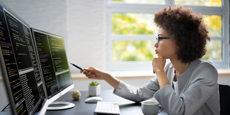 African American woman pointing to multiple desktop screens, thinking.