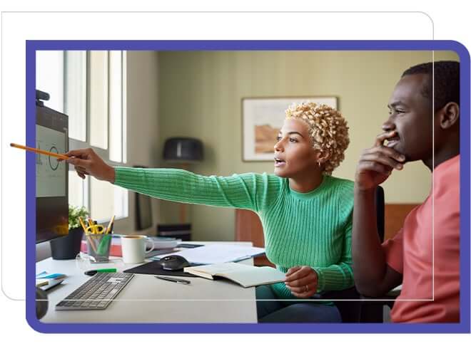 woman in green sweater points out info to man in pink shirt on screen