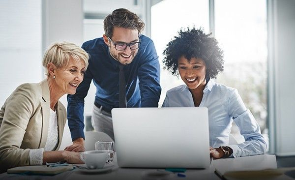 Three professionals are gathered around a laptop, engaged in a collaborative work discussion. 